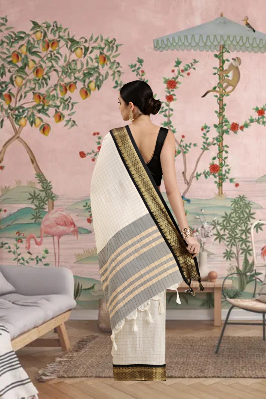 Woman in a saree standing in a room with a decorative wall mural featuring animals and plants.