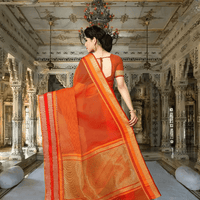 Model in orange saree with golden borders, standing gracefully
