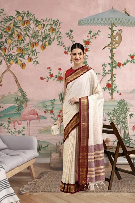 Front view of white checkered cotton silk saree with maroon border in regal setting
