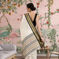 Woman in a saree standing in a room with a decorative wall mural featuring animals and plants.